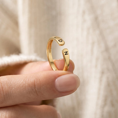 Bague à initiales or tenue entre les doigts